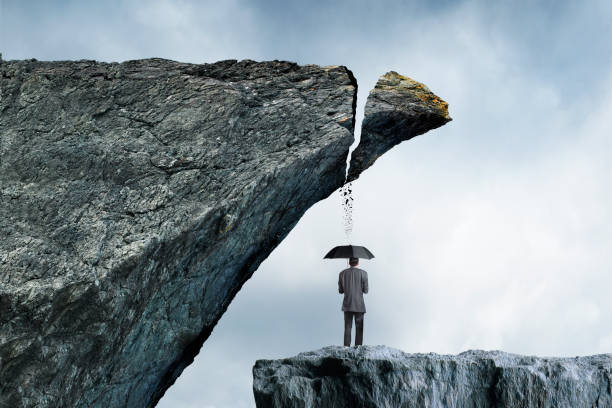 A man holding an umbrella as his only protection stands as part of a cliff is breaking off and is about to fall on top of him.