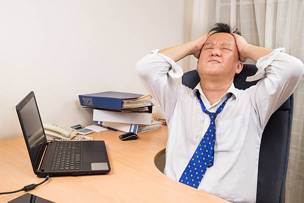Frustrated, stressful and tired Asian business manager seated behind desk in office