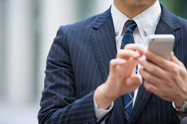 An Asian (Japanese) businessman contacting using a smartphone on the street of a business district