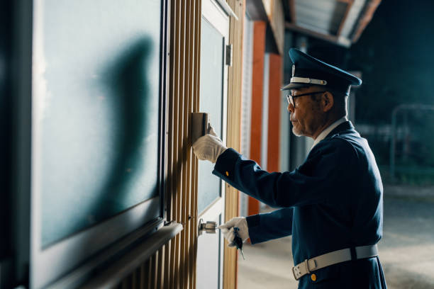 Senior male security guard unlocking a door while on duty at night in Japan